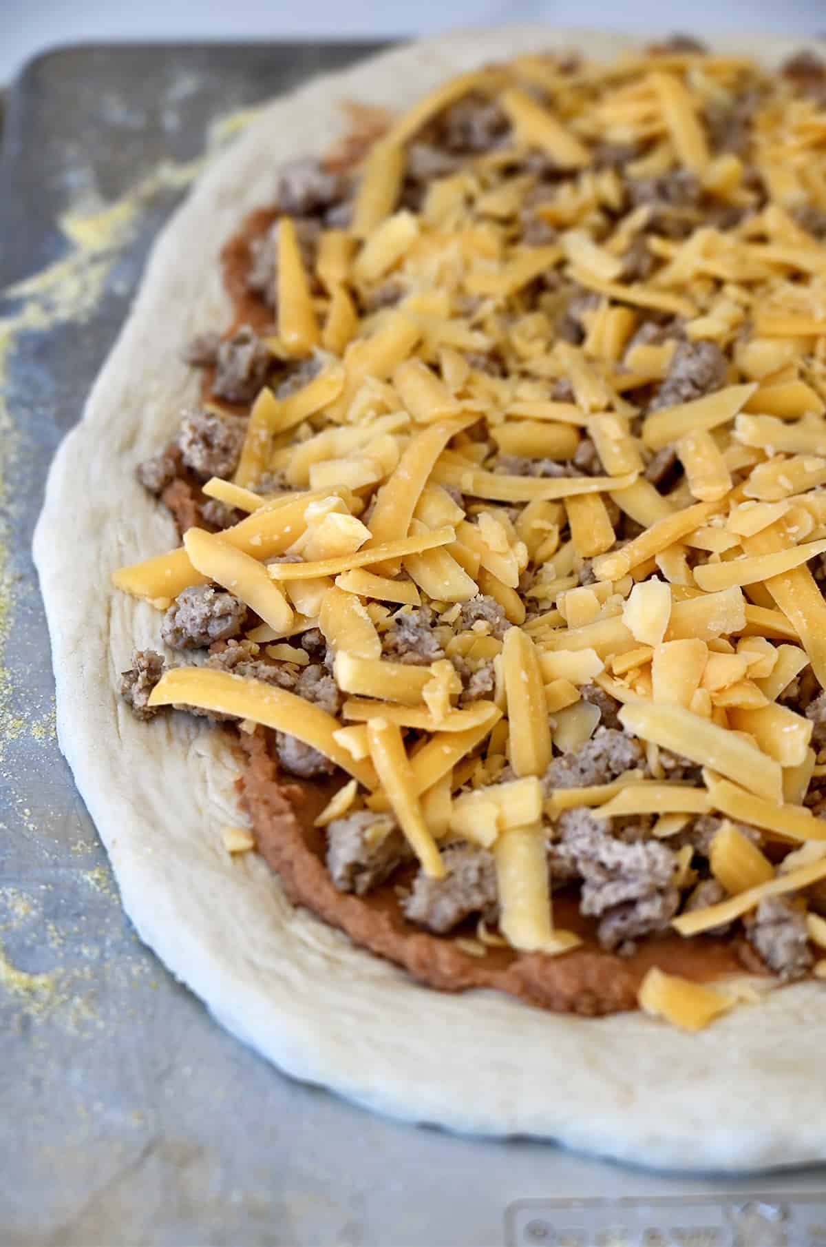 Pizza dough topped with refried beans, cooked taco meat and shredded cheddar cheese.