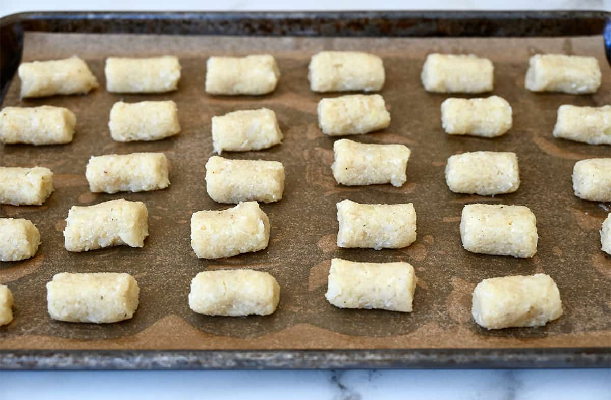 Unbaked cauliflower tots on a parchment paper-lined baking sheet.