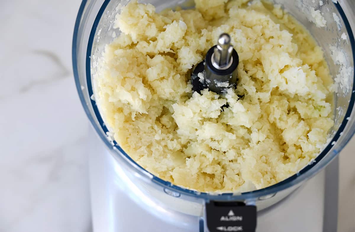 Cauliflower that's been pulsed to fine pieces in a bowl of a food processor.