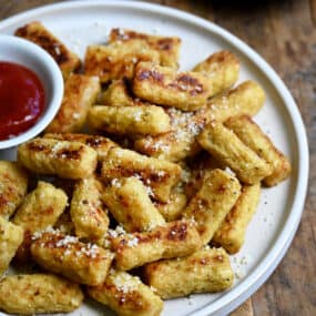 A pile of cauliflower tots on a plate with a small bowl containing ketchup.