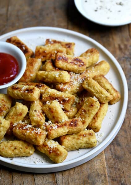 A pile of cauliflower tots on a plate with a small bowl containing ketchup.