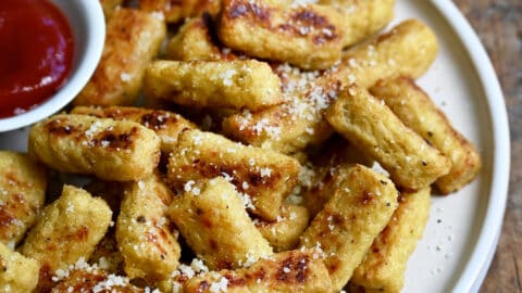 A pile of cauliflower tots on a plate with a small bowl containing ketchup.