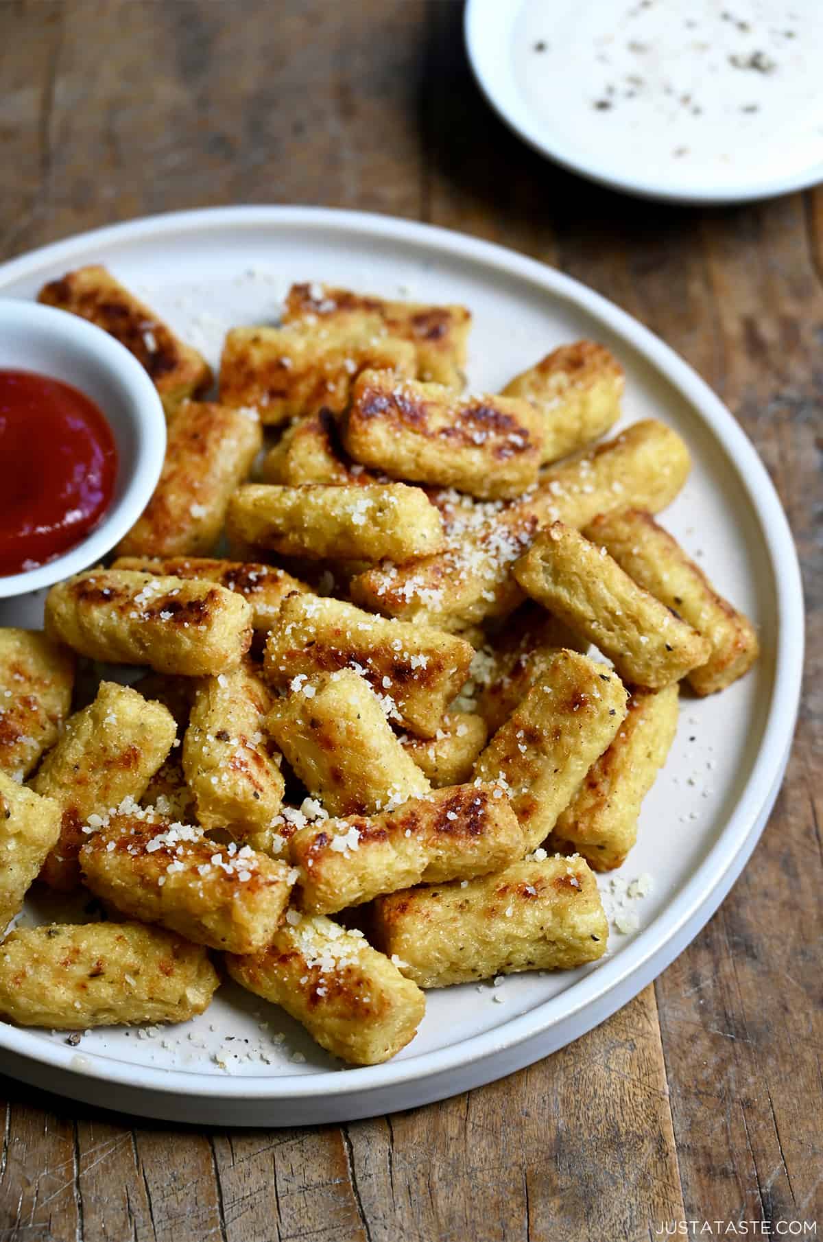 A pile of cauliflower tots on a plate with a small bowl containing ketchup.