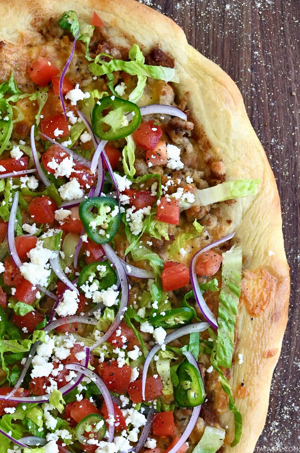 Cheesy chicken taco pizza topped with fresh toppings, including shredded lettuce, diced tomatoes and jalapeños, and crumbled cojita cheese.