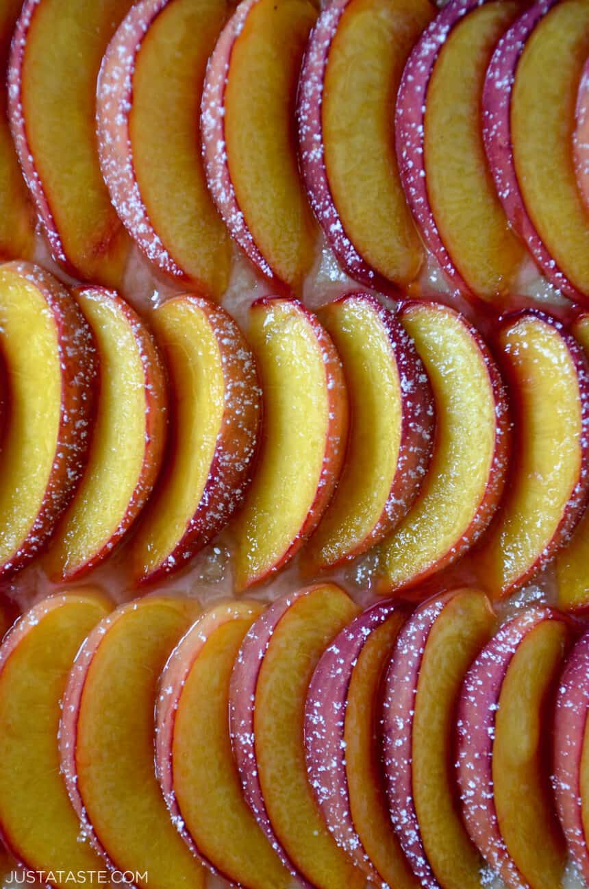 A closeup view of fresh peach slices in three perfect rows dusted with powdered sugar.