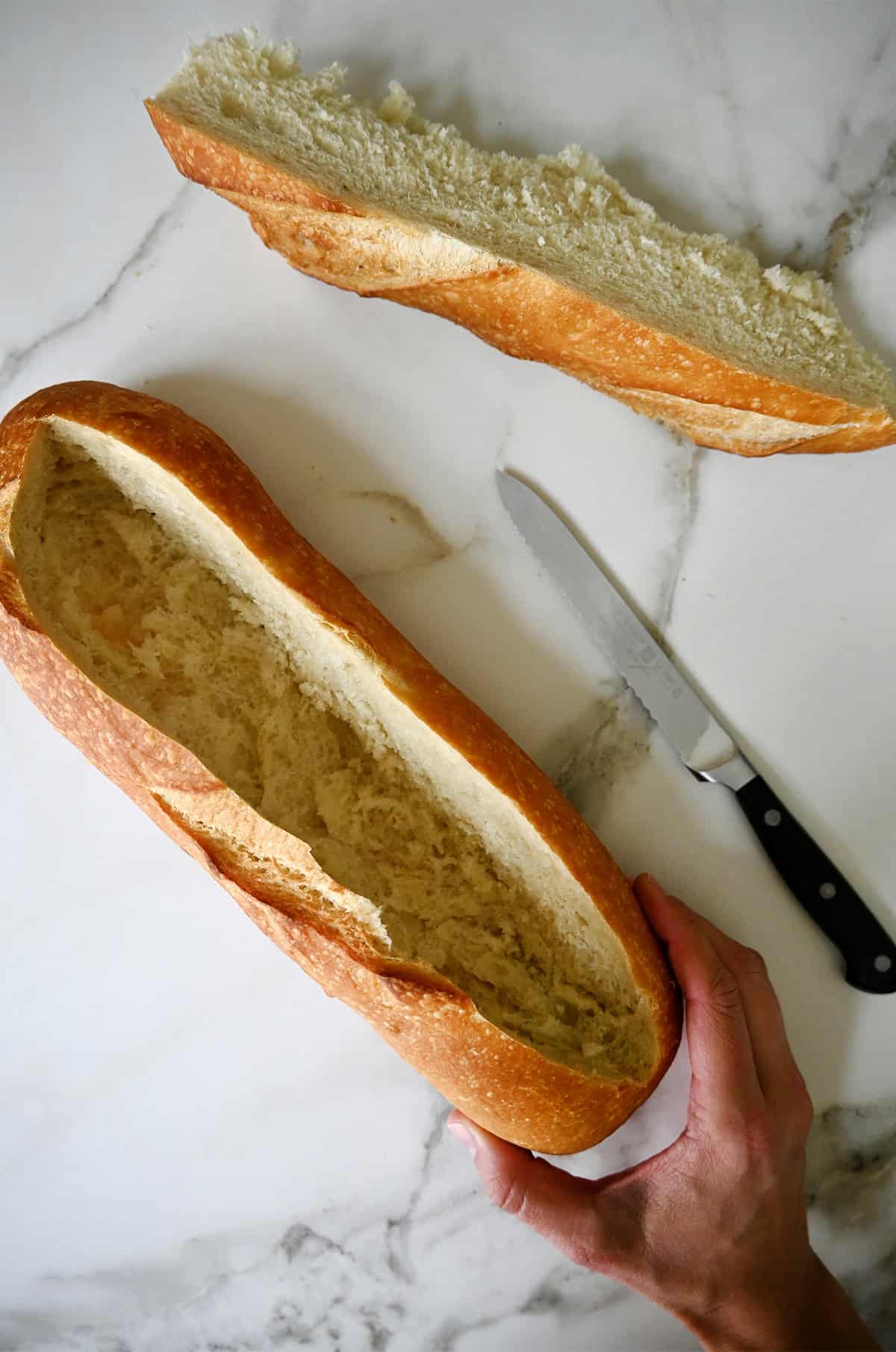 A hand holds a loaf of bread with a deep "V" cut out of the center. A sharp knife and the cut out center are nearby.