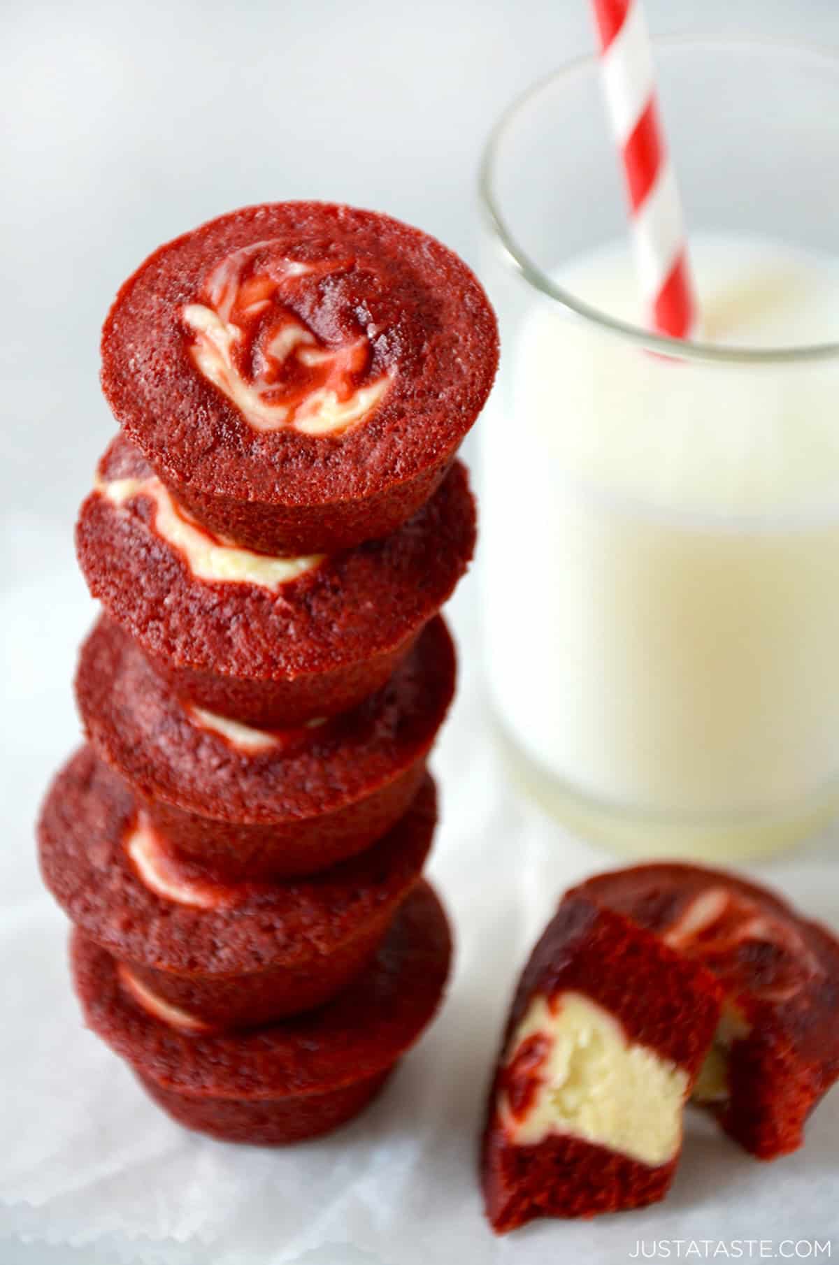 Red velvet cheesecake brownie bites stacked five high next to a glass of milk.