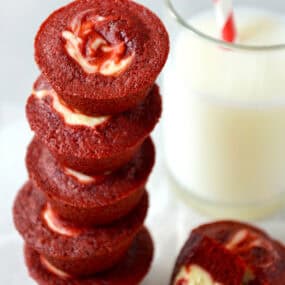 Red velvet cheesecake brownie bites stacked five high next to a glass of milk.