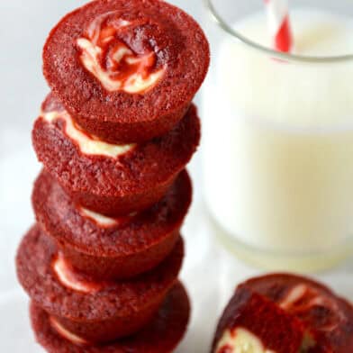 Red velvet cheesecake brownie bites stacked five high next to a glass of milk.