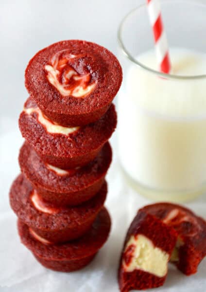 Red velvet cheesecake brownie bites stacked five high next to a glass of milk.