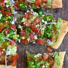 Cheesy taco pizza topped with refried beans, shredded lettuce, jalapeños, cojita cheese and diced tomatoes.