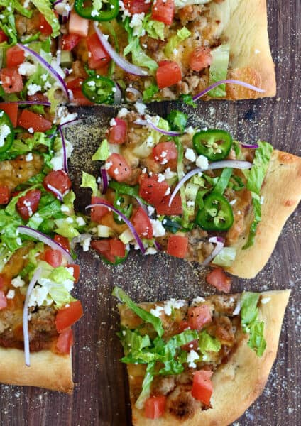 Cheesy taco pizza topped with refried beans, shredded lettuce, jalapeños, cojita cheese and diced tomatoes.