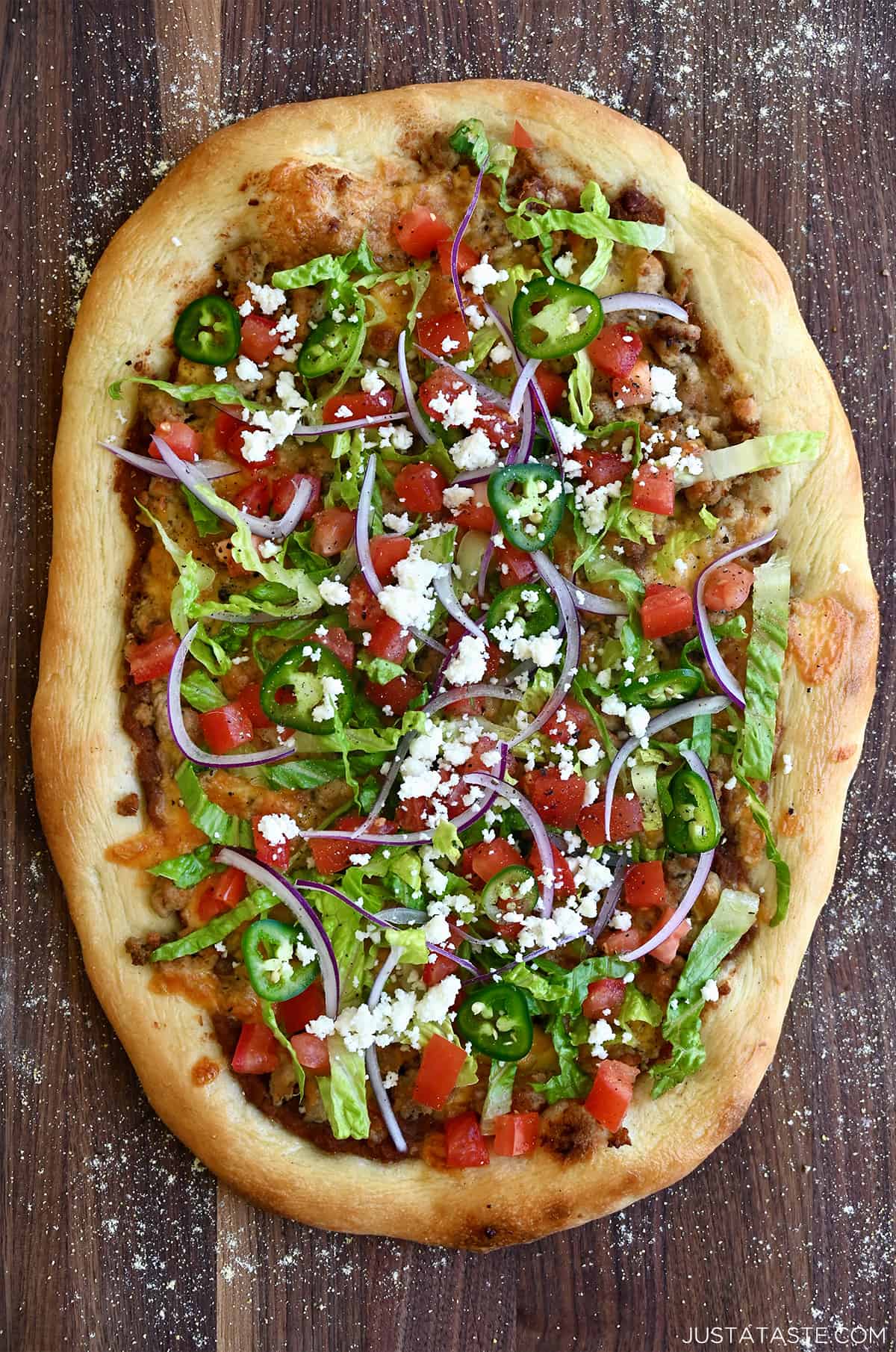 Taco pizza with ground chicken, refried beans, cheddar cheese, diced tomatoes, sliced red onions, shredded lettuce and crumbled cojita cheese.