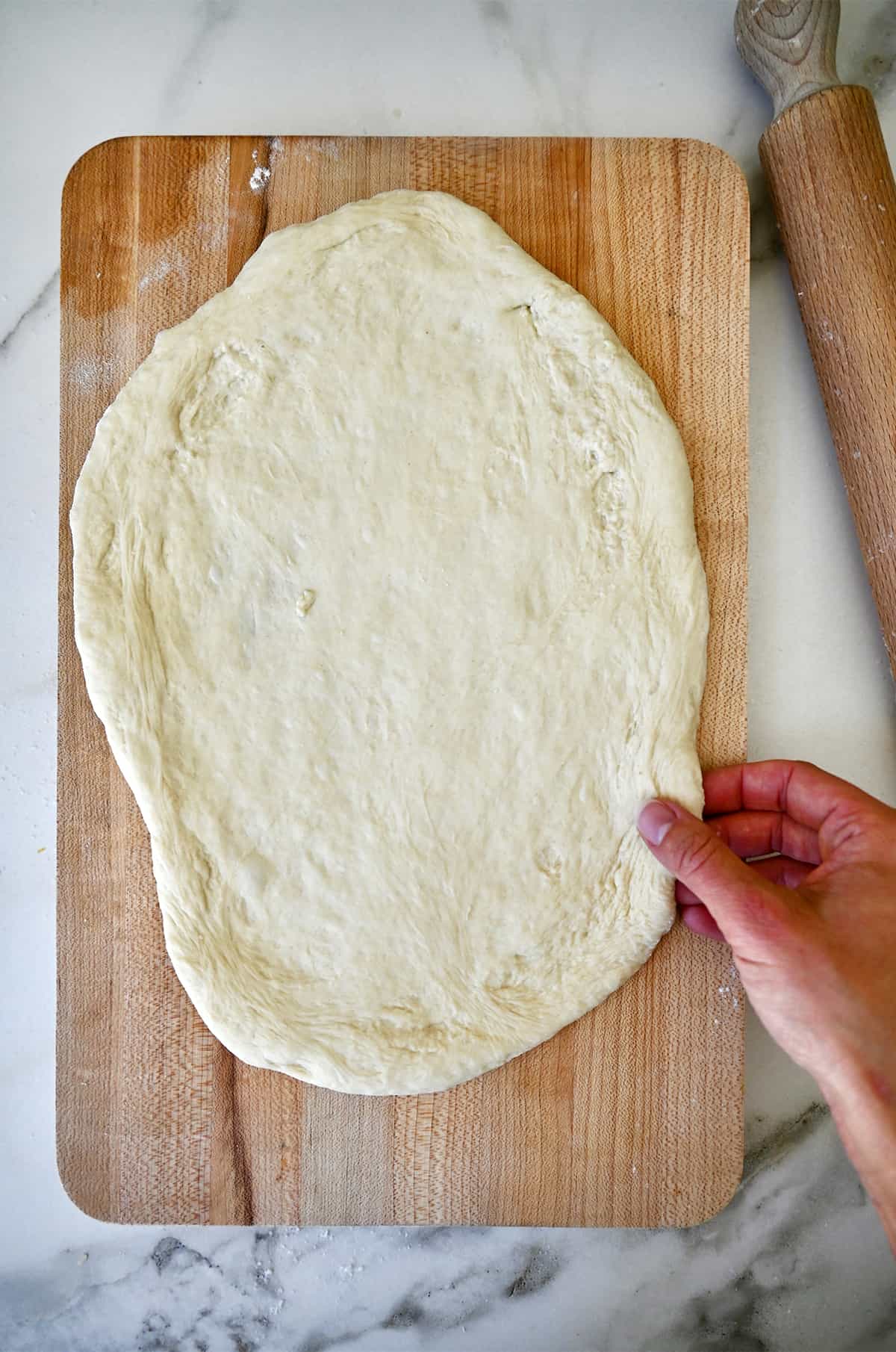 Pizza dough on a wood cutting board next to a rolling pin.