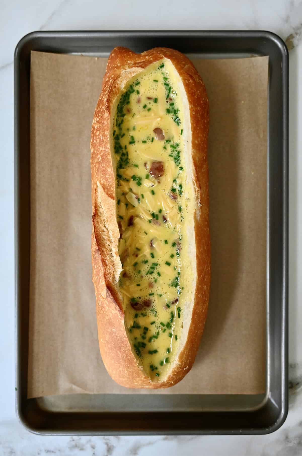 An unbaked bread boat with scrambled eggs in the center on a parchment paper-lined baking sheet.