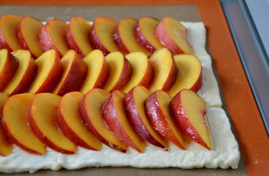 Puff pastry topped with rows of fresh stone fruit slices.