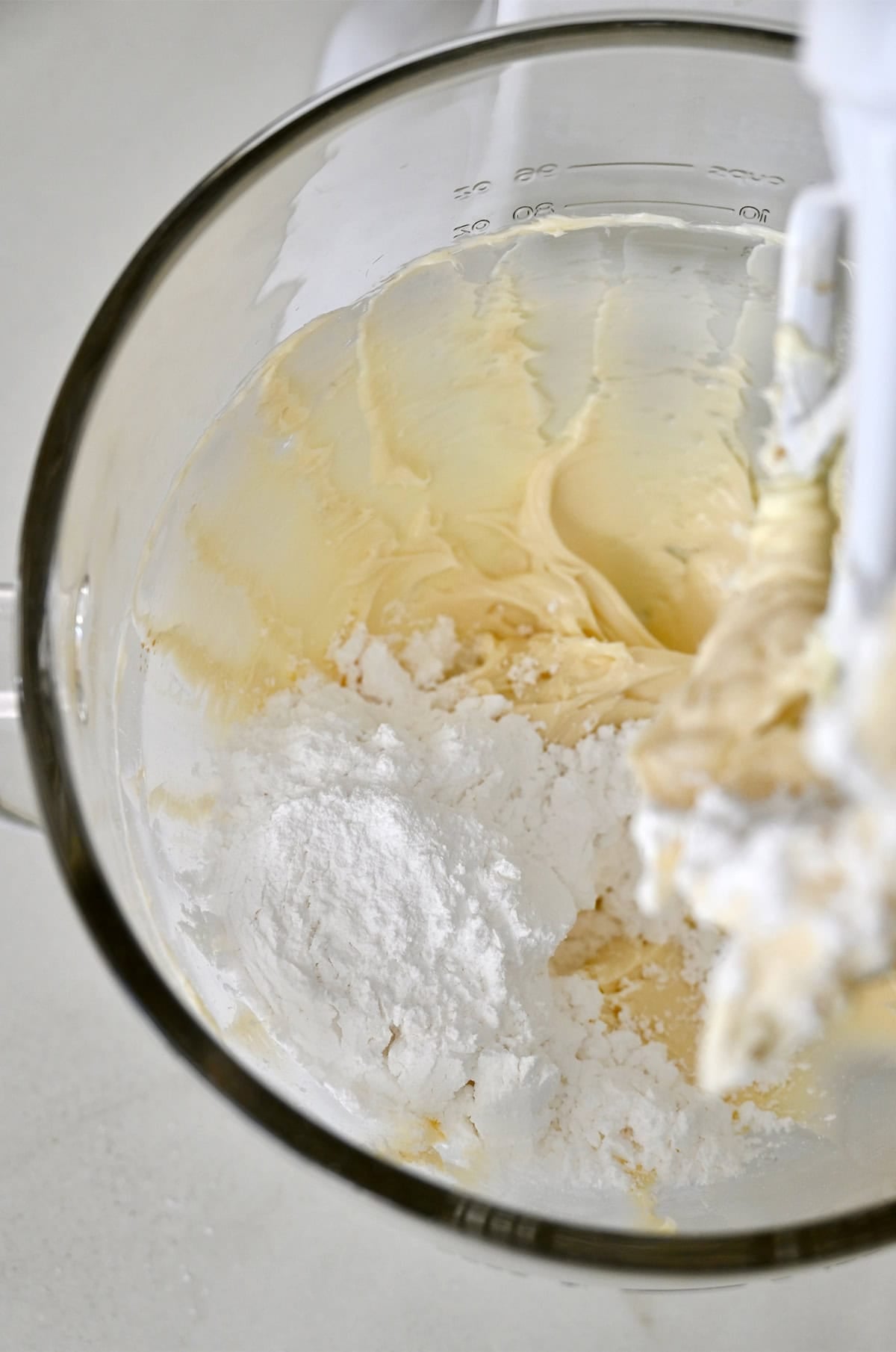 Sifted powdered sugar in a mixing bowl with a creamy butter and vanilla mixture.