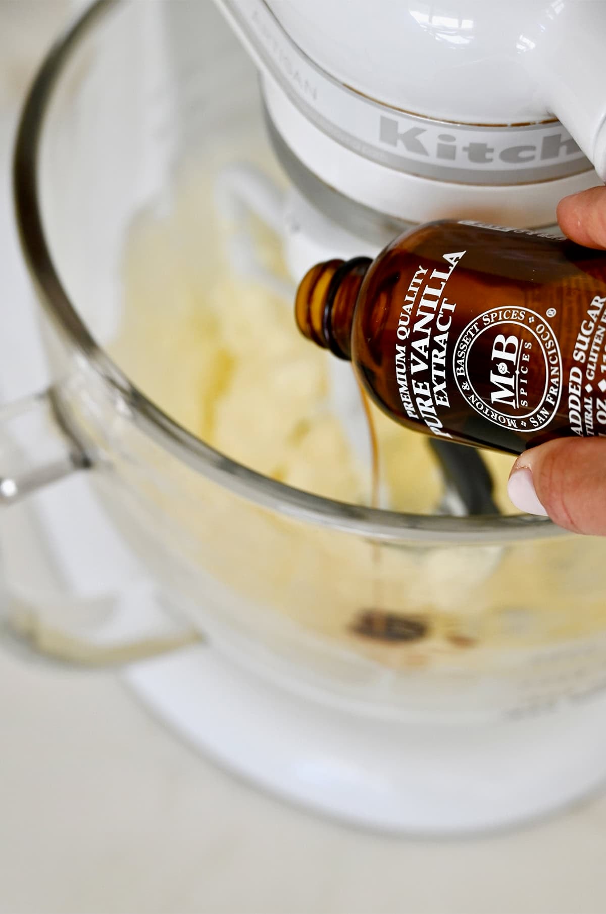Adding vanilla extract to a stand mixer bowl with creamy beaten butter.