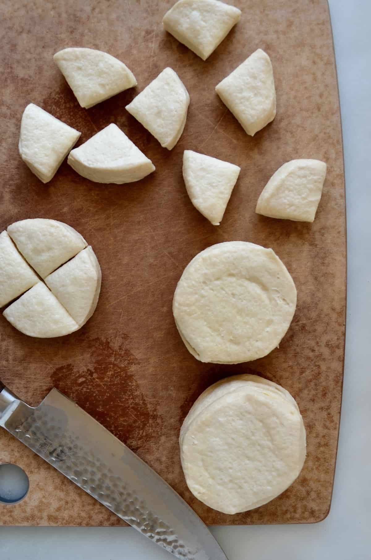 Canned biscuit dough cut into pieces on a wood cutting board with a chef knife.