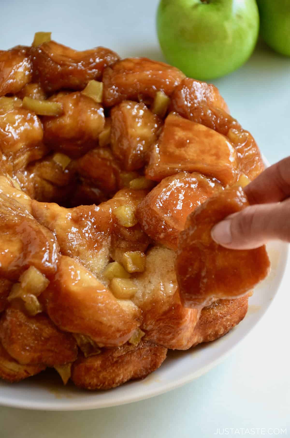 A hand pulls at a piece of caramel apple monkey bread that's on a white serving plate.