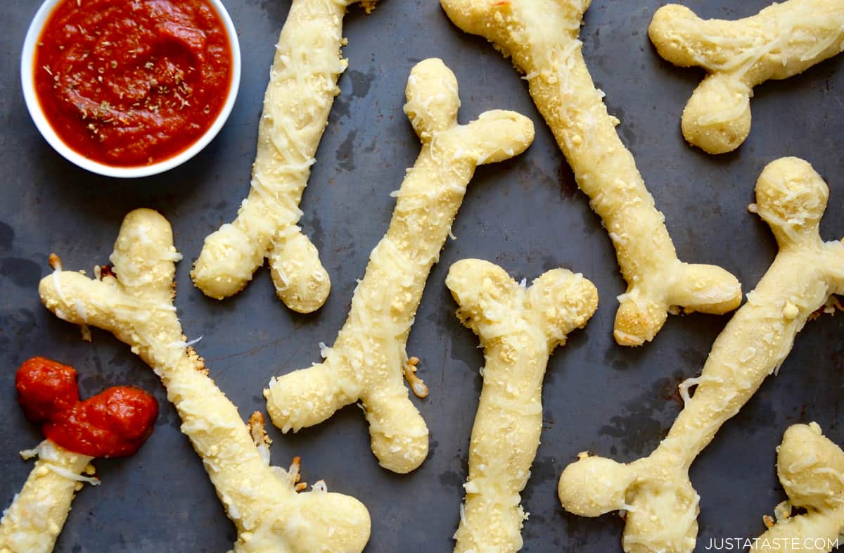 Cheesy breadsticks in the shape of bones next to a small bowl containing marinara sauce. 