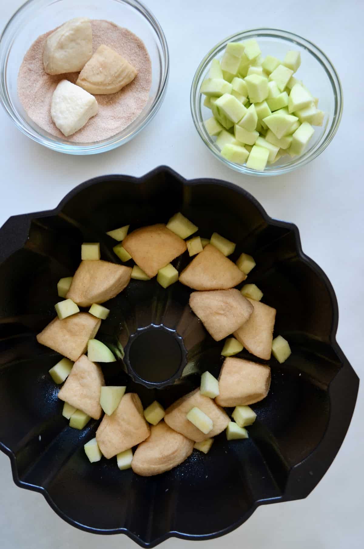 A bundt pan containing diced Granny Smith apples and pieces of canned biscuit dough.