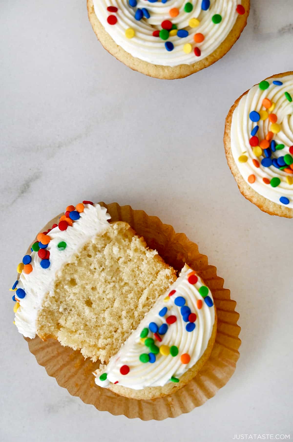 A vanilla cupcake with vanilla buttercream and confetti sprinkles cut in half.
