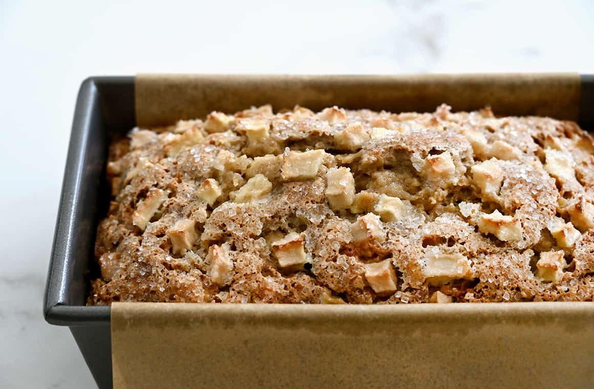 Golden brown banana bread studded with diced apples in a parchment paper-lined loaf pan