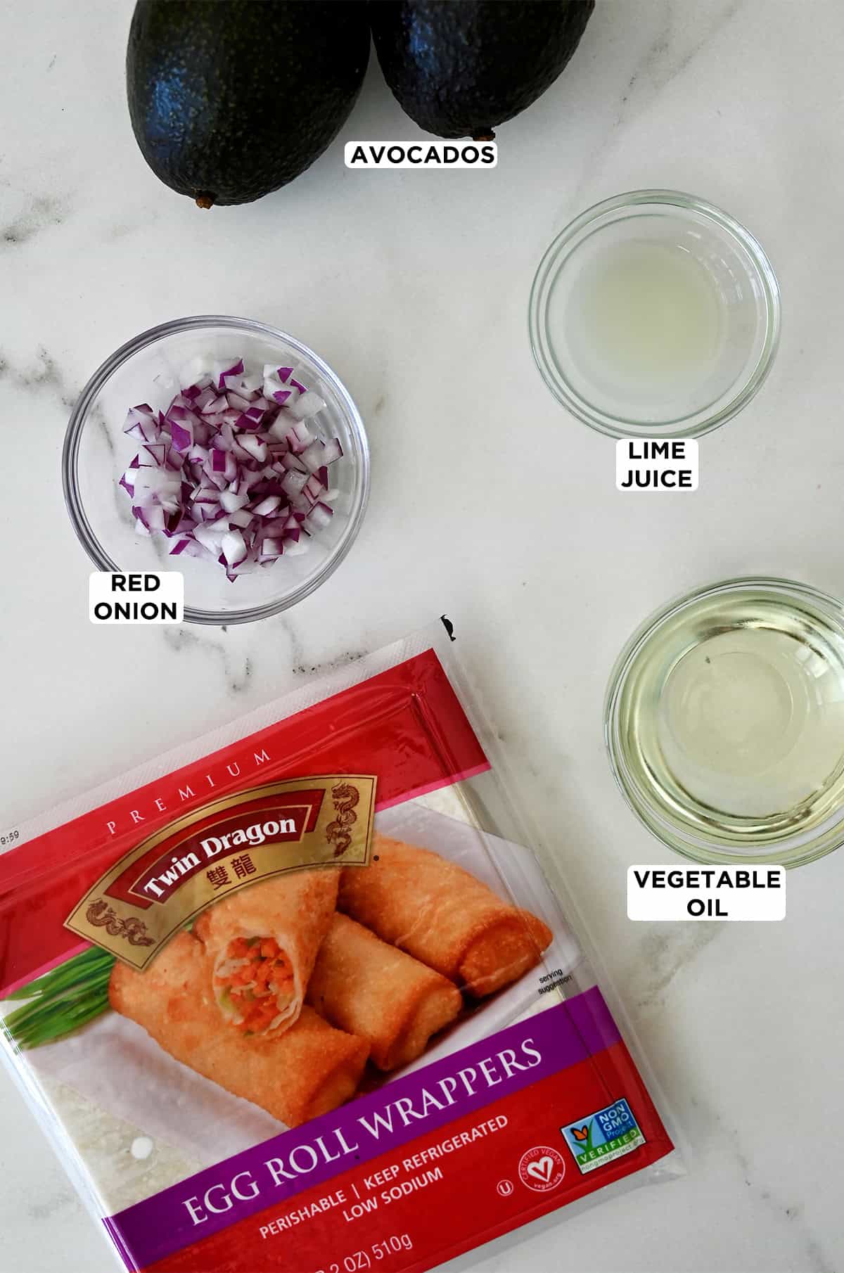 Egg roll wrappers next to glass bowls containing diced red onion, lime juice and vegetable oil, plus two ripe avocados.