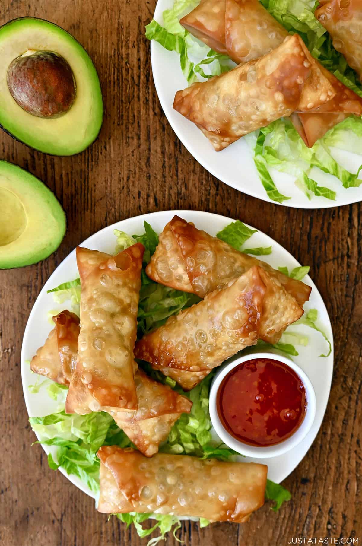 Avocado egg rolls atop shredded lettuce on a plate with a small bowl containing sweet chili sauce.
