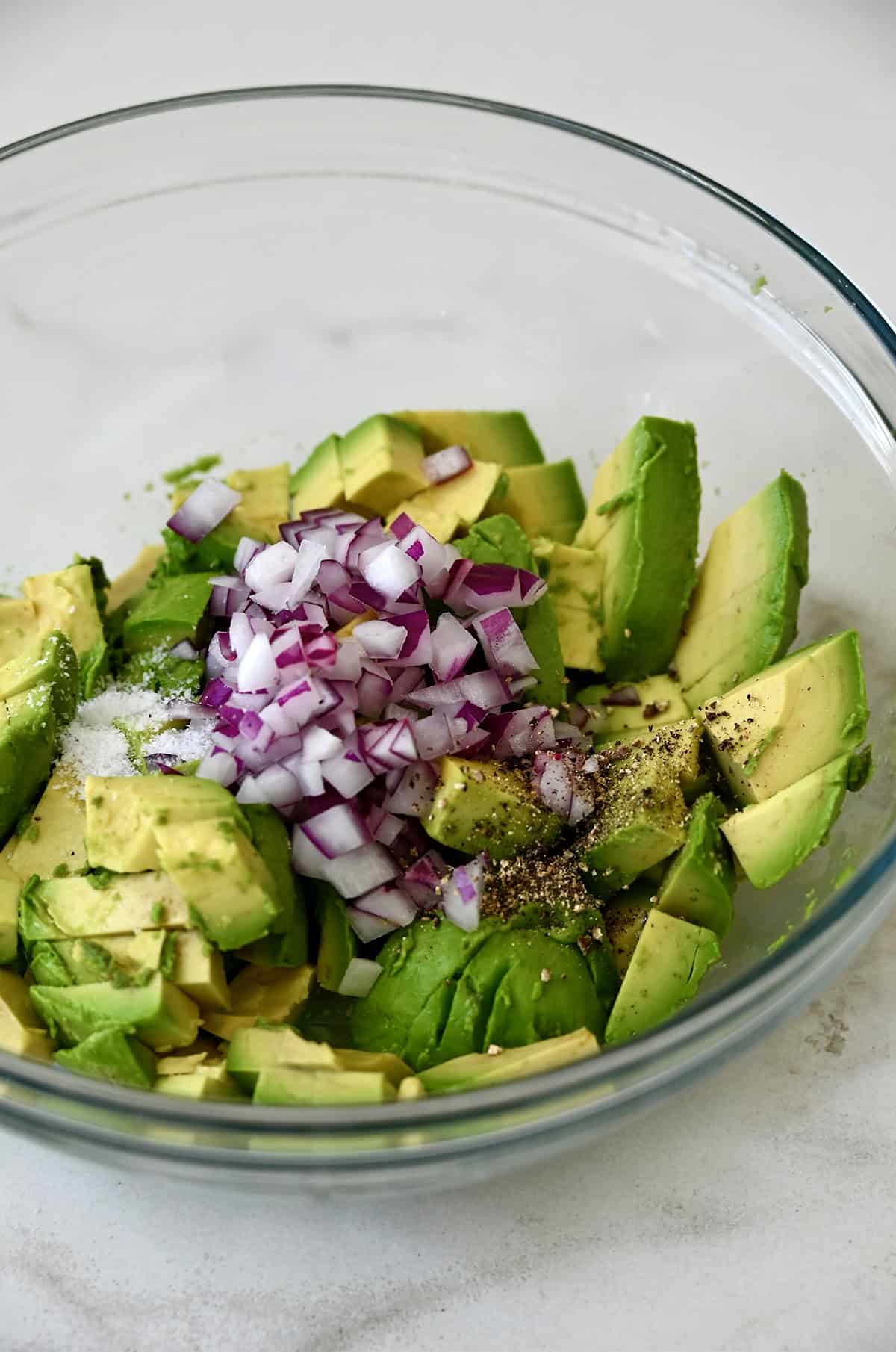 Diced red onions and avocado in a glass bowl.