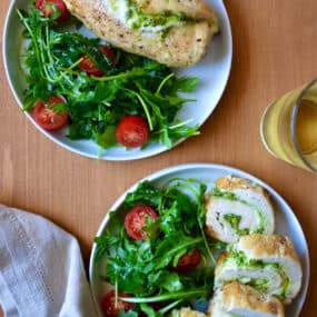 Sliced chicken roulades filled with pesto are on a plate with a salad of greens and tomatoes.