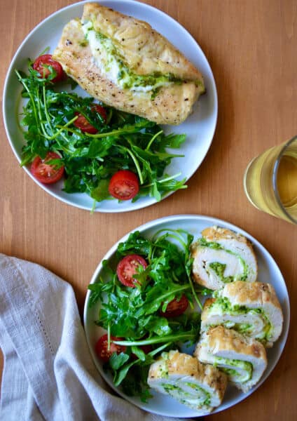 Sliced chicken roulades filled with pesto are on a plate with a salad of greens and tomatoes.