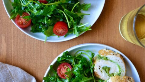Sliced chicken roulades filled with pesto are on a plate with a salad of greens and tomatoes.