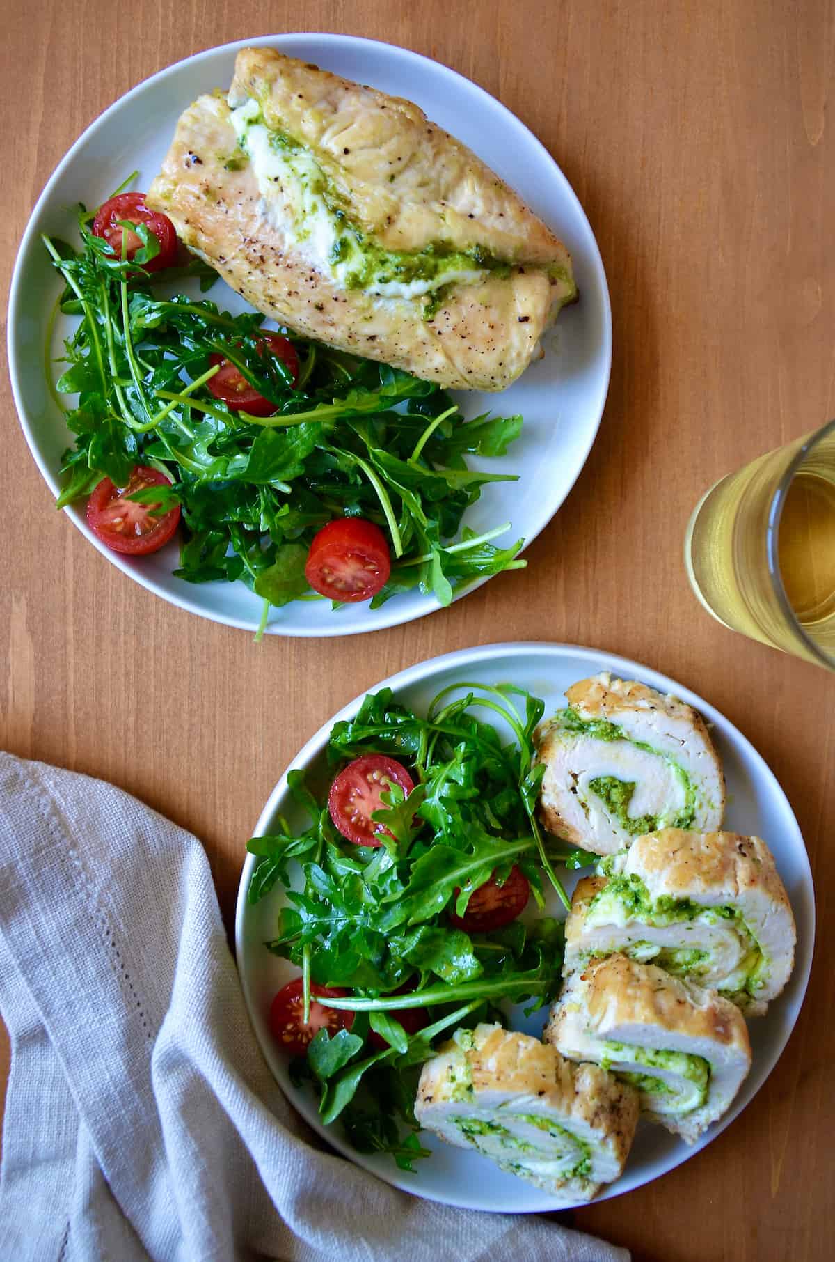 Sliced chicken roulades filled with pesto are on a plate with a salad of greens and tomatoes.