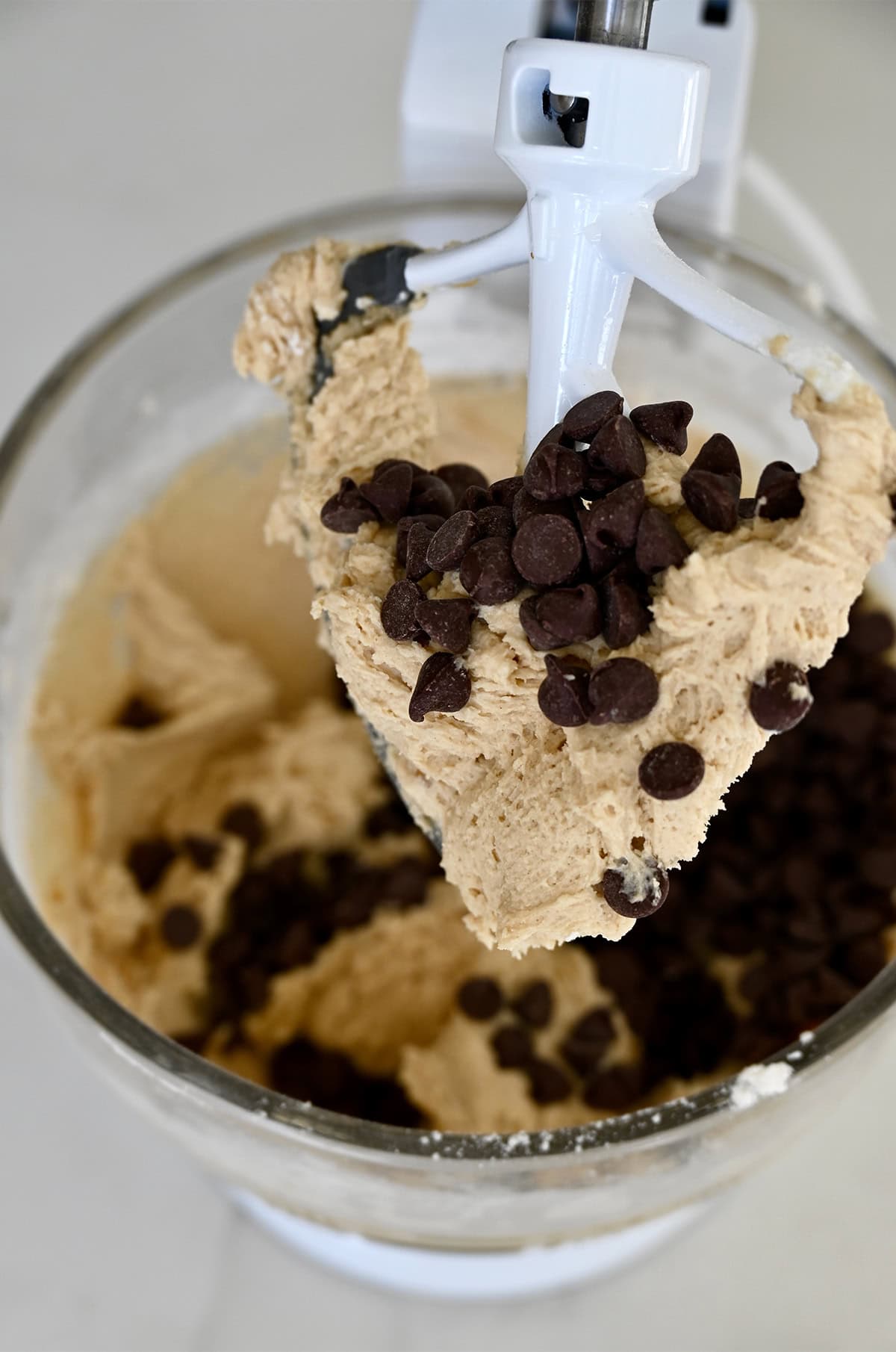 Chocolate chip cookie dough covering the paddle attachment of a stand mixer.