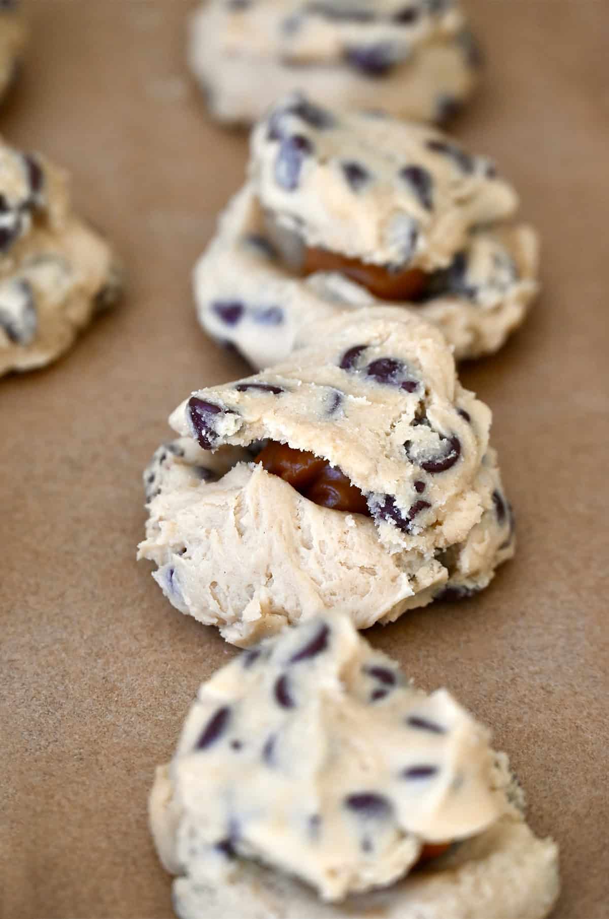 Cookie dough balls stuffed with soft caramels on a baking sheet lined with parchment paper.