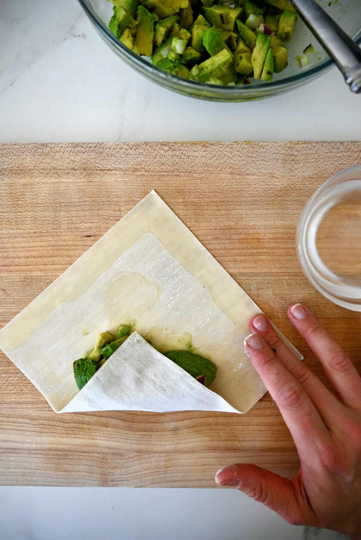 The first fold to making an egg roll, the bottom portion is folded over an avocado filling.