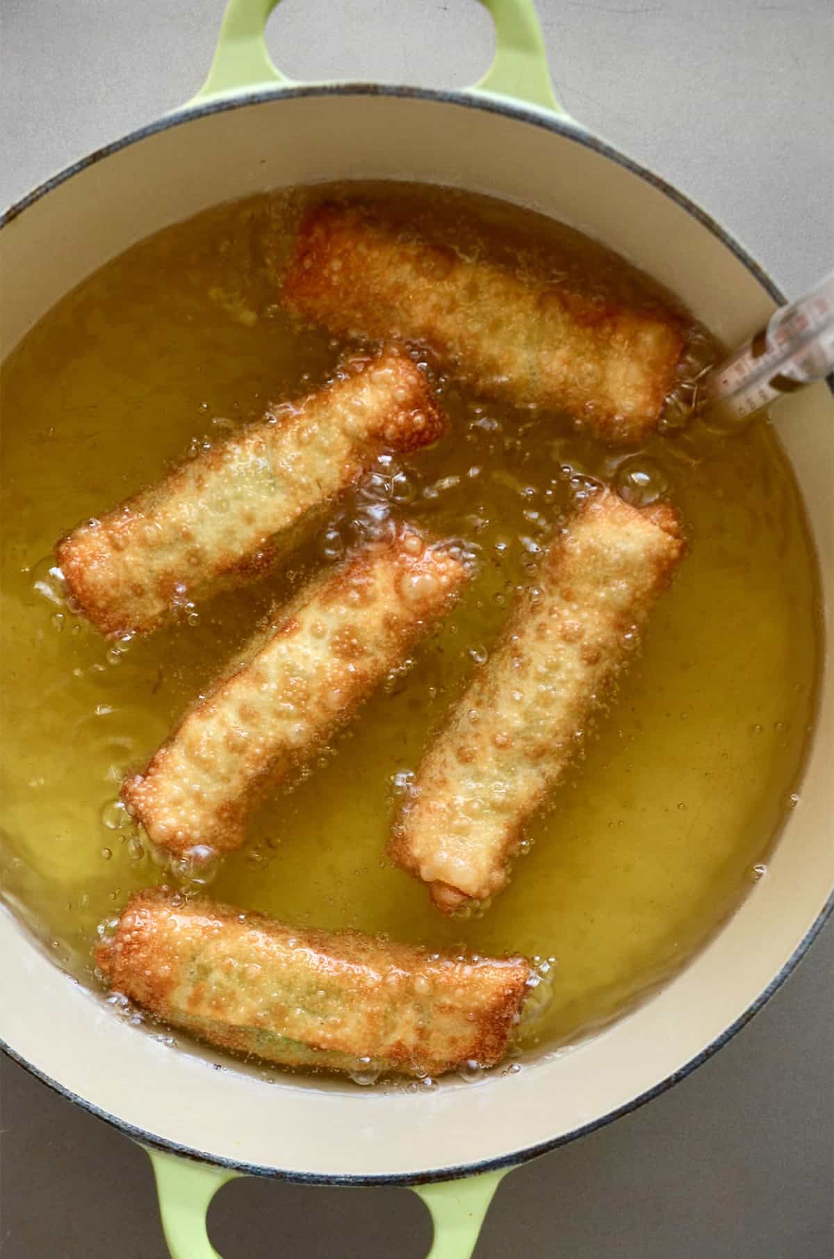 Avocado egg rolls frying in oil.