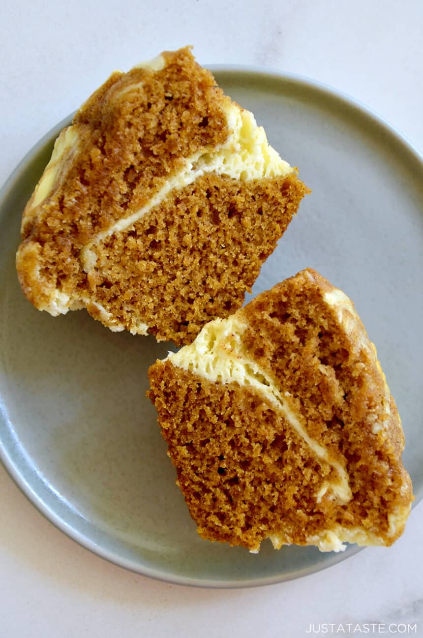 A pumpkin muffin with cream cheese cut in half on a plate