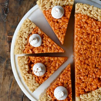 Pumpkin Rice Krispie treats cut into pie wedges and topped with a dollop of whipped cream.