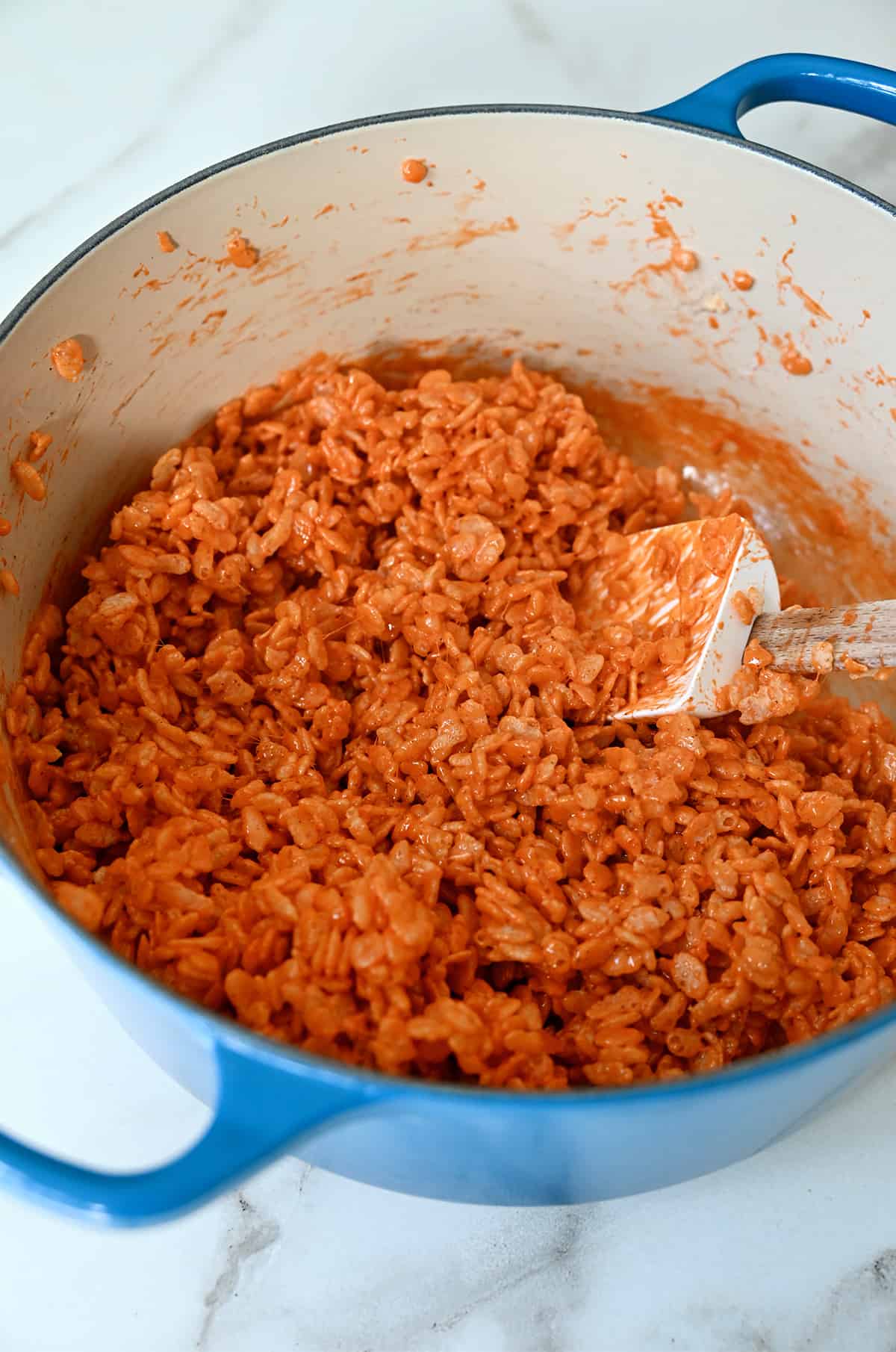 A large stockpot containing orange-colored Rice Krispies and a spatula.