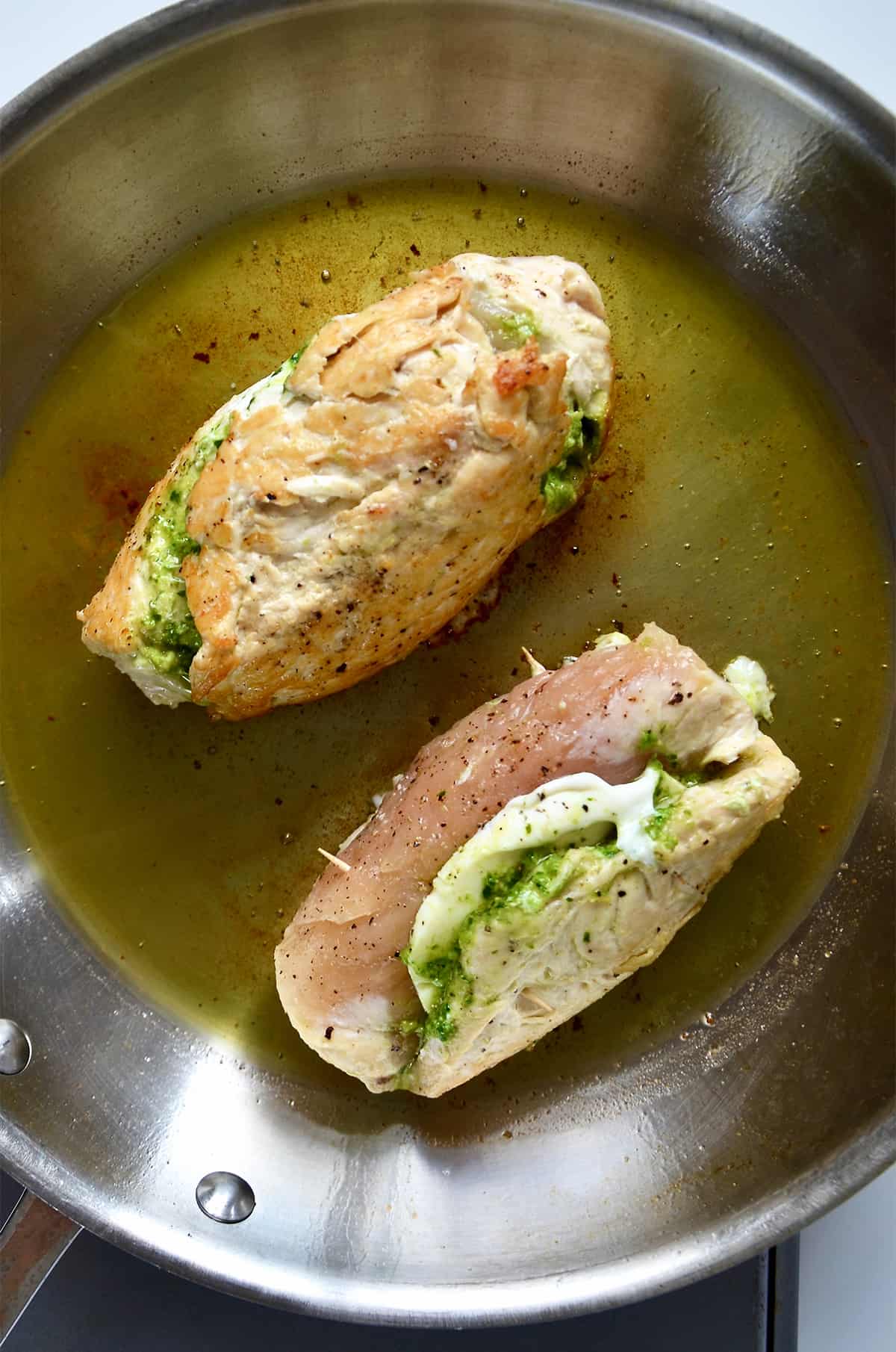 Pesto and mozzarella-stuffed chicken breasts are cooking in a skillet.