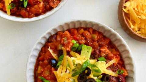 Two bowls containing 30-Minute Leftover Turkey Chili topped with sour cream, diced avocado, black olives and shredded cheddar cheese