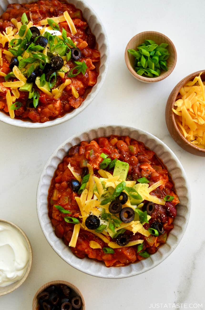 Two bowls containing 30-Minute Leftover Turkey Chili topped with sour cream, diced avocado, black olives and shredded cheddar cheese