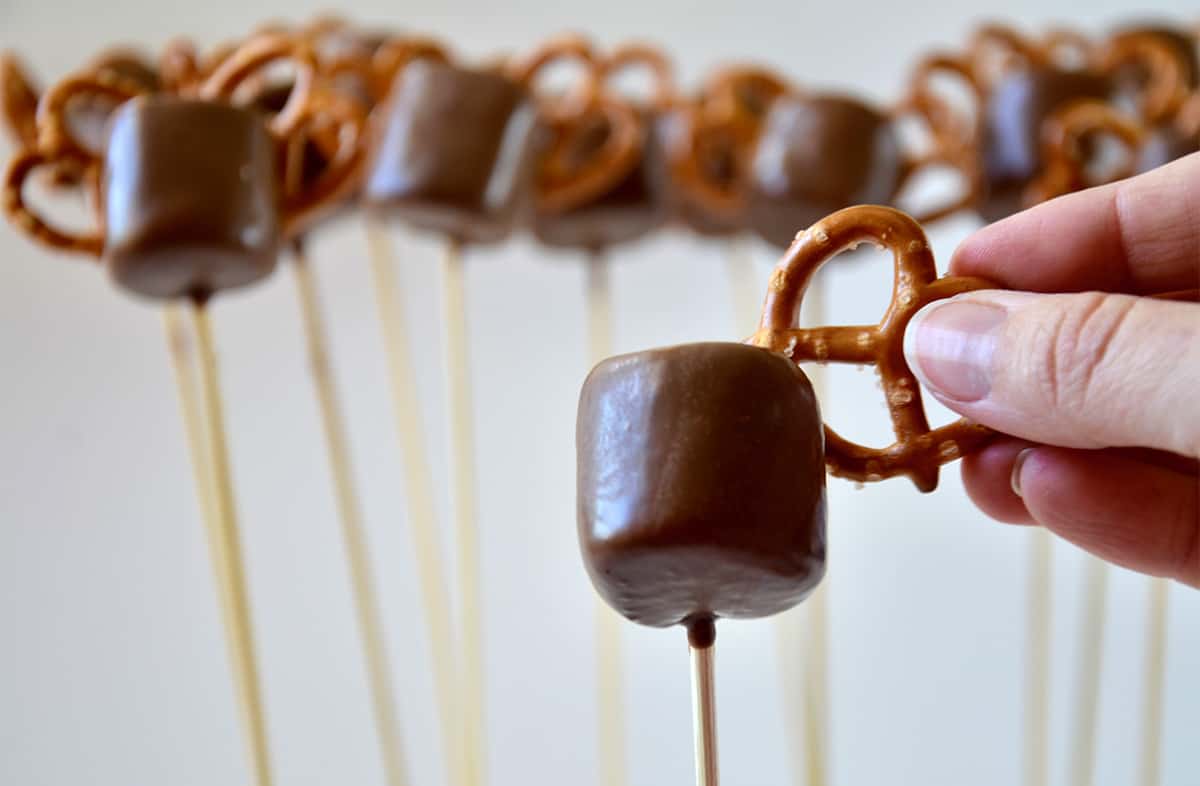 A hand attaches a small pretzel to a chocolate-covered marshmallow.