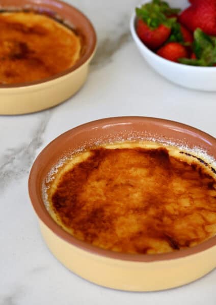 Two ramekins containing creme brulee cheesecakes with a burnt sugar topping.