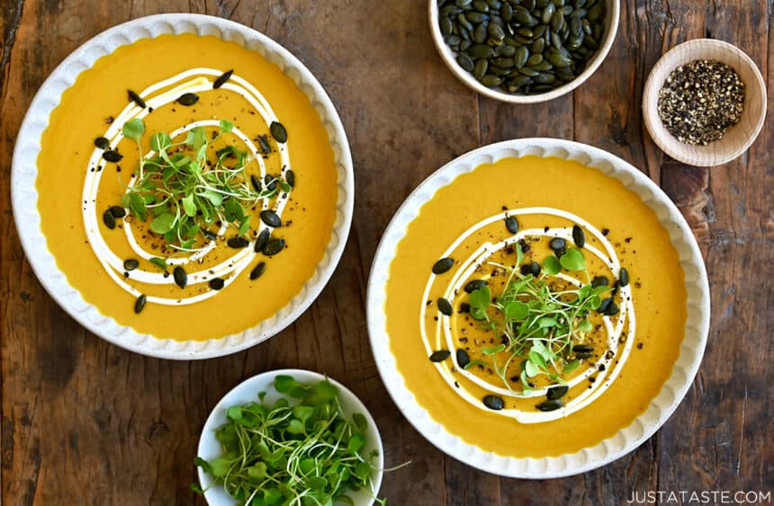 A top-down view of two bowls containing easy Thai coconut pumpkin soup garnished with micro greens, toasted pumpkin seeds and a drizzle of sour cream