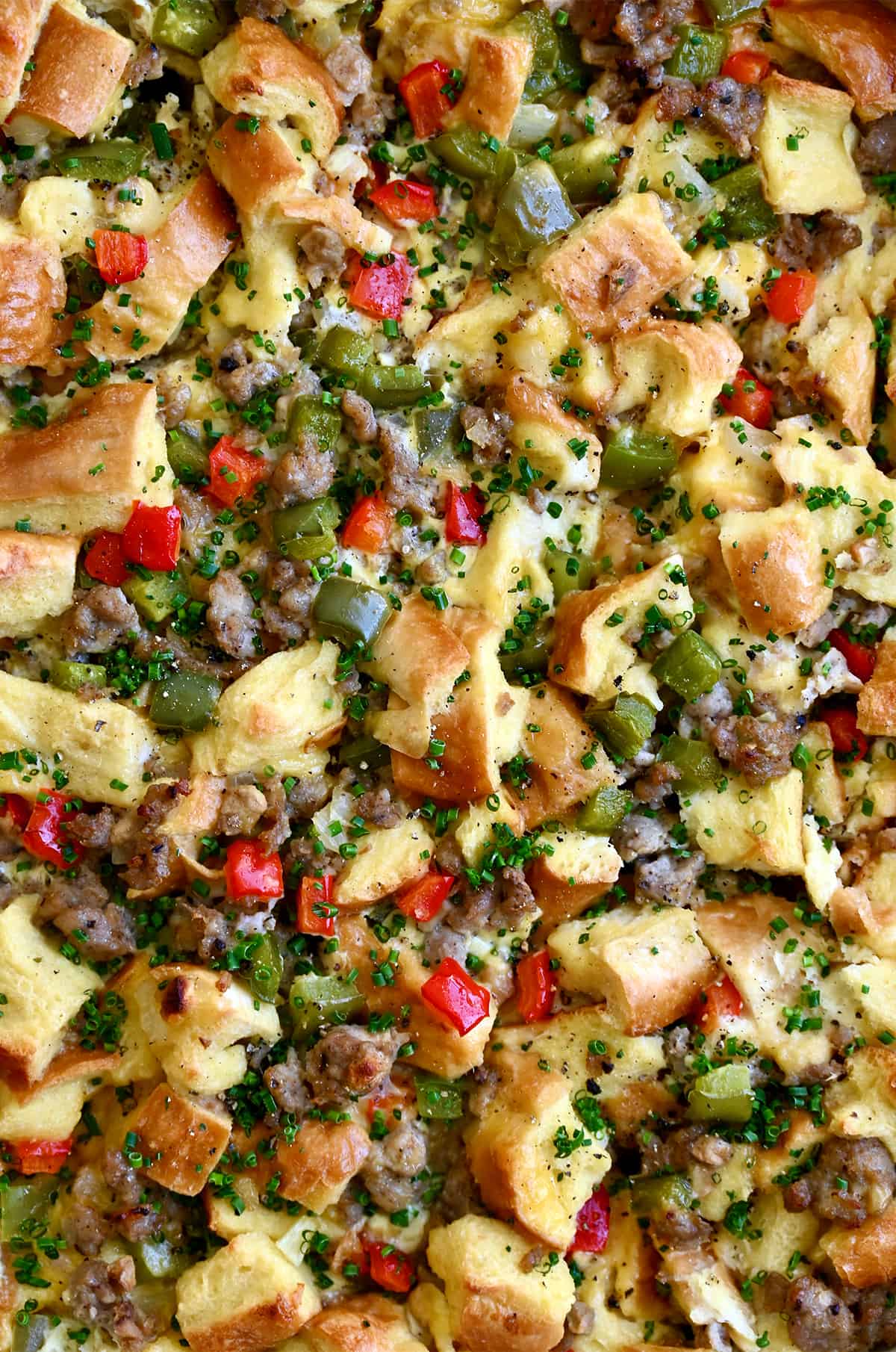 A closeup view of egg breakfast casserole with cubed French bread, sausage and diced veggies.