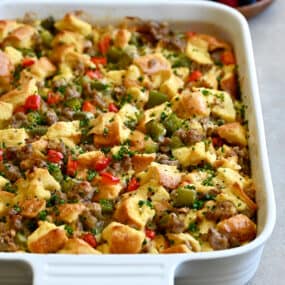 An egg casserole with breakfast sausage and colorful bell peppers in a white baking dish next to a bowl of fresh berries.